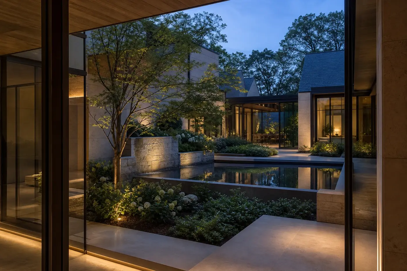 Private landscaped courtyard with limestone walls, a reflecting basin, and bronze-framed glass at twilight