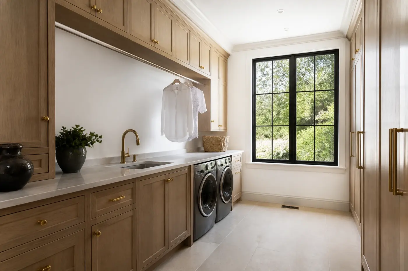 New Charlotte luxury custom-home laundry room with white oak cabinetry, side-by-side machines, a stone counter, utility sink, and garden window