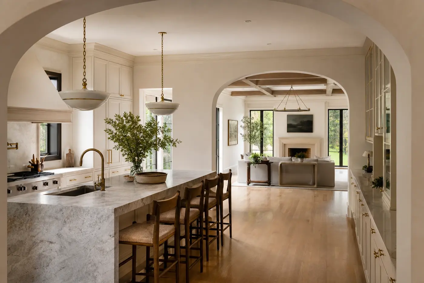 Renovated luxury kitchen with natural stone island, inset cabinetry, plaster archways, and connected family room