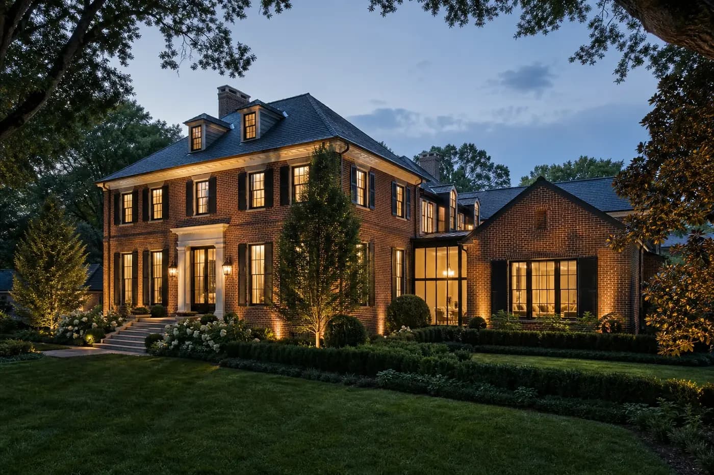 Renovated classic brick Charlotte estate with a seamless modern addition and landscaped gardens at dusk